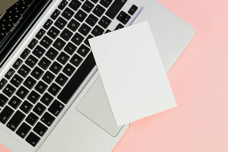 A blank card placed on a laptop keyboard with ample copy space on a pastel background.